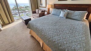 A hotel room with a large bed, a chair, a small table, and a view of the city through large windows. - Luau 6533 South Facing Gulf Views! |Wifi | Tram Included (Miramar Beach)