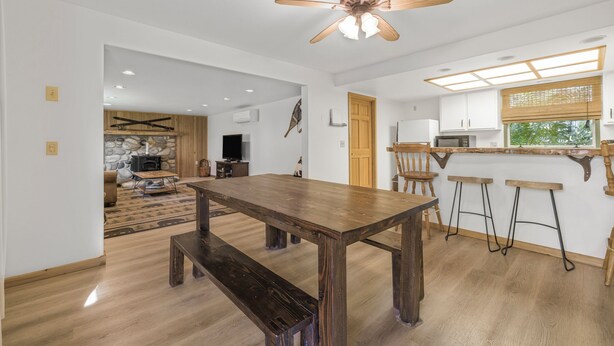Un vaste espace de vie comprenant un coin repas avec une table en bois, un ventilateur de plafond et une cuisine équipée de tabourets de bar.