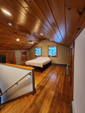 Una stanza con pavimento in legno, un letto, una scrivania, una sedia e una scala.