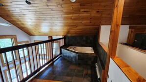 Una escalera de madera que lleva a un baño con bañera y pared de piedra.