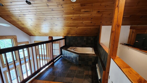 A wooden staircase leading to a bathroom with a bathtub and a stone wall.