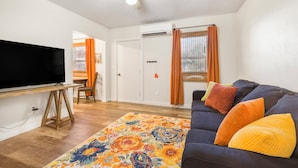 A living room with a flat-screen TV, a ceiling fan, a sofa with colorful cushions, and a floral rug. - Salmon River Cabin #210 (Riggins)