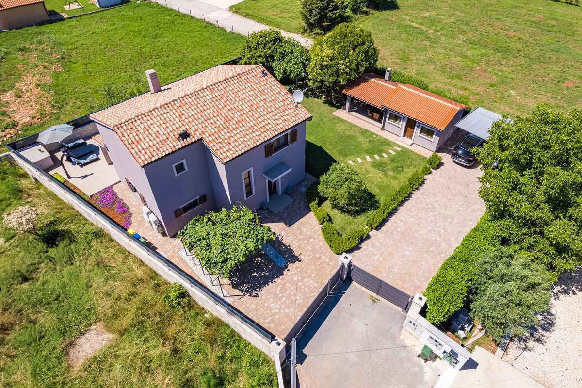 An aerial view of a two-story house with a tiled roof, a covered patio, and a driveway.