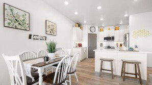 Une cuisine moderne avec des meubles blancs, un îlot central et un coin repas comprenant des chaises blanches et une table en bois.
