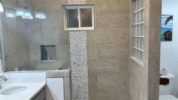 A bathroom with a double sink, a shower with a glass door, and a toilet.