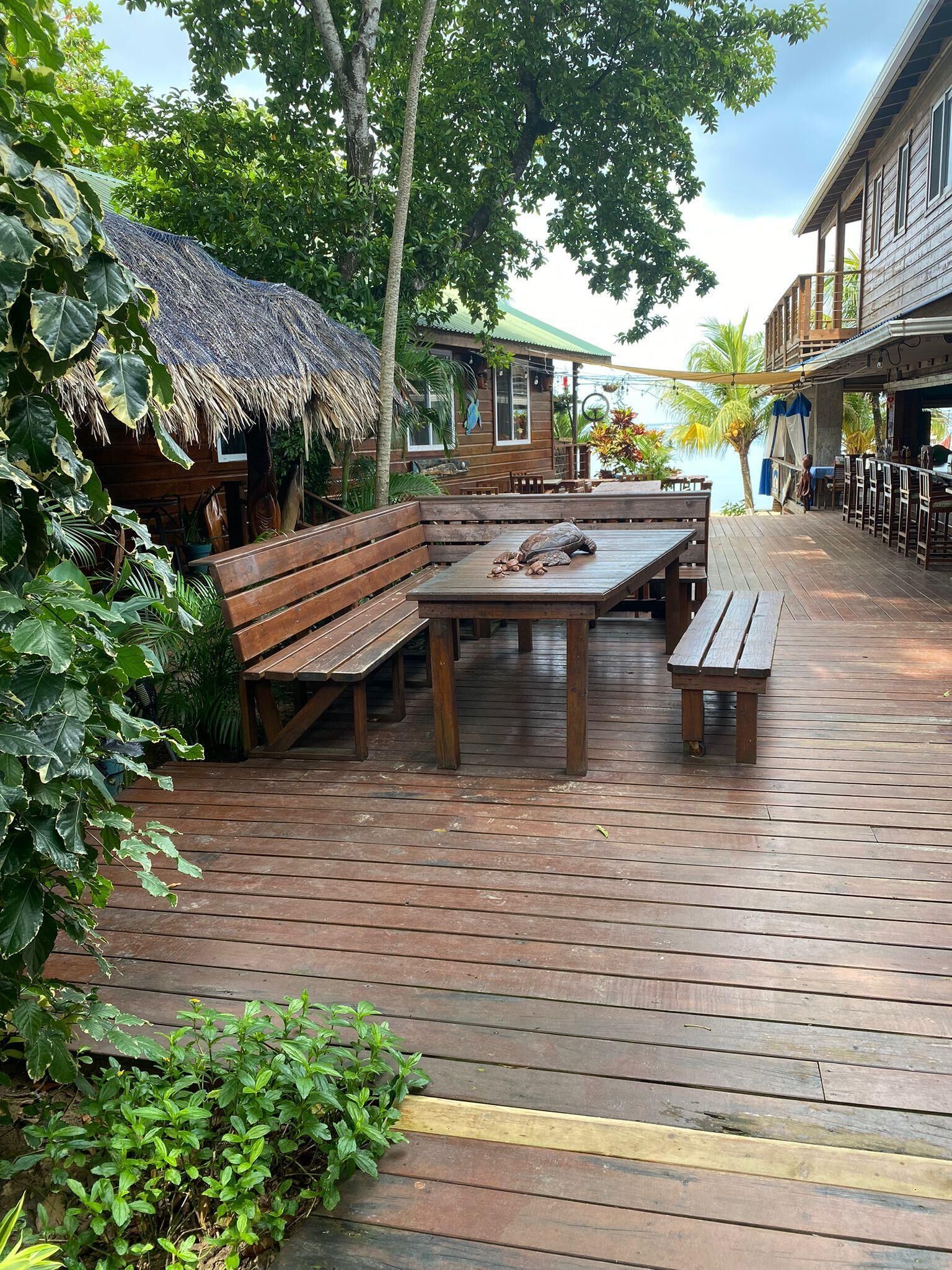 Une terrasse extérieure en bois, dotée d’un espace salon, d’une structure à toit de chaume et offrant une vue sur la mer.