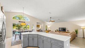 Una cocina moderna con armarios grises, una isla grande y un comedor con vista a la piscina.