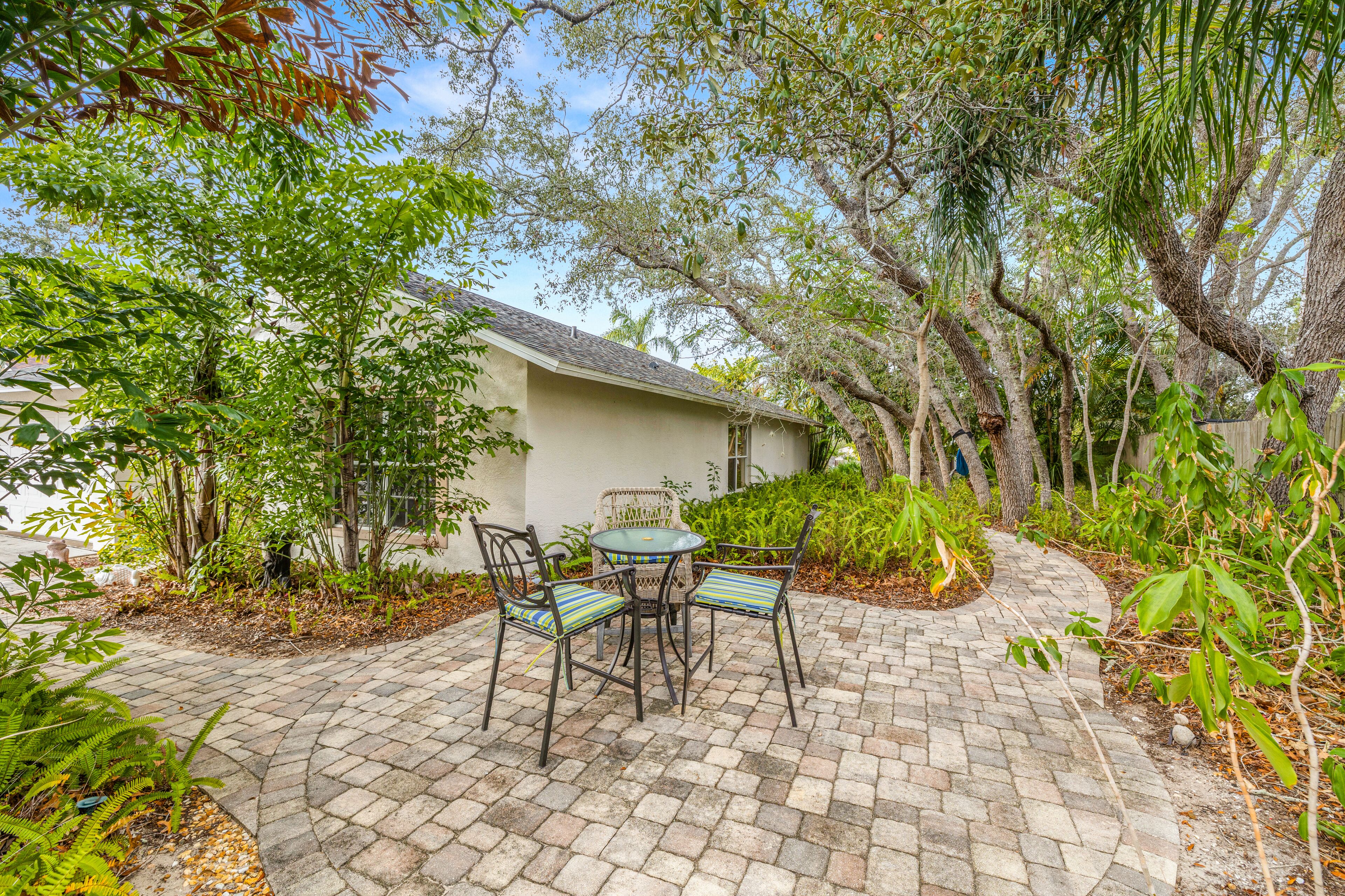 A patio area with a table and chairs, surrounded by lush greenery and trees.