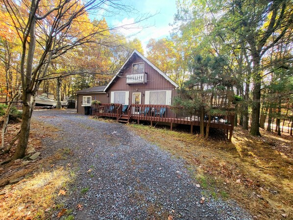 Une cabane dotée d’une véranda, entourée d’arbres et bordée d’un chemin de gravier.