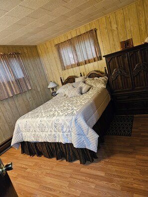 Une chambre à coucher avec une tête de lit en bois, un lit avec une literie à motifs, une table de chevet avec une lampe et une armoire en bois.