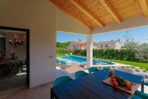 Zona de menjador a l'aire lliure coberta, amb piscina i vista al jardí.