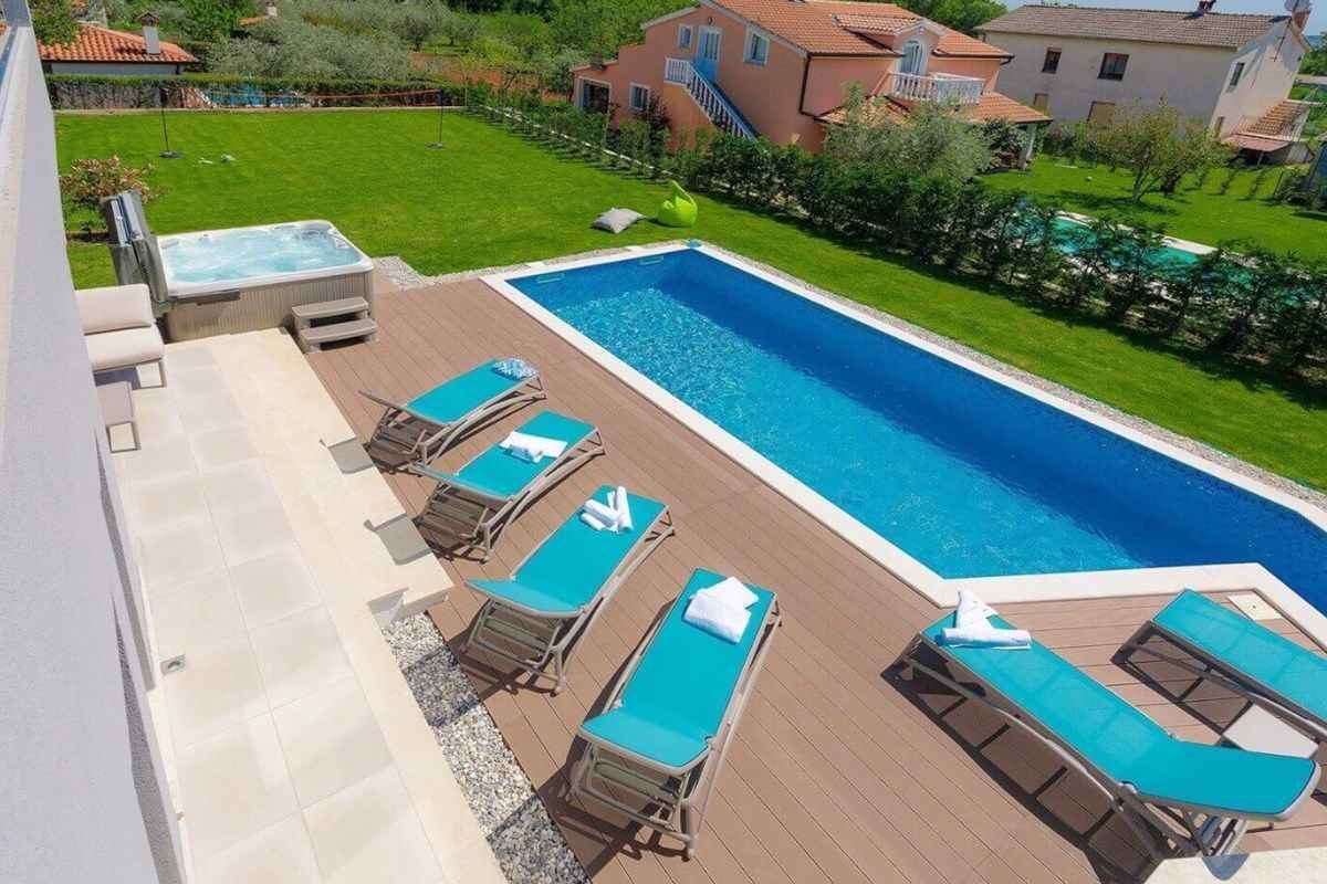 Zwembad met ligbedden en een jacuzzi op een houten terras.