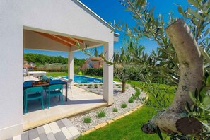 Terrassa exterior moderna amb piscina, envoltada d'oliveres i un jardí ben cuidat.
