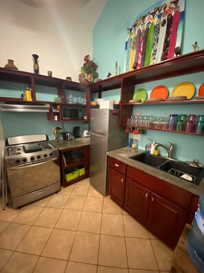 Kitchen features a gas stove, microwave, refrigerator, and sink, with ample storage and a shelf for glassware and dishes.