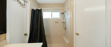 A bathroom with a shower, a window, and a door.