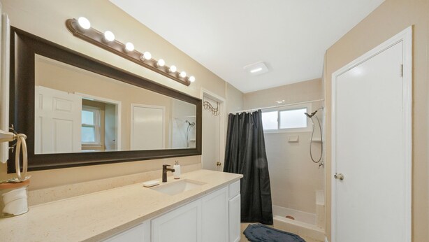A bathroom with a vanity, sink, mirror, and shower.