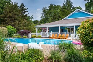 A house with a blue roof, a covered porch with white railings, and a swimming pool with lounge chairs. - Harbor Breeze - year round swimming (South Haven)