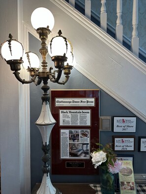 A chandelier with multiple lights, a framed newspaper article, and a plaque on a wall.