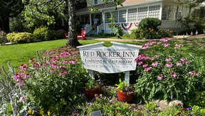 Schild des Red Rocker Inn in Black Mountain, N.C., umgeben von einem Garten mit verschiedenen Blumen und einem Haus im Hintergrund.