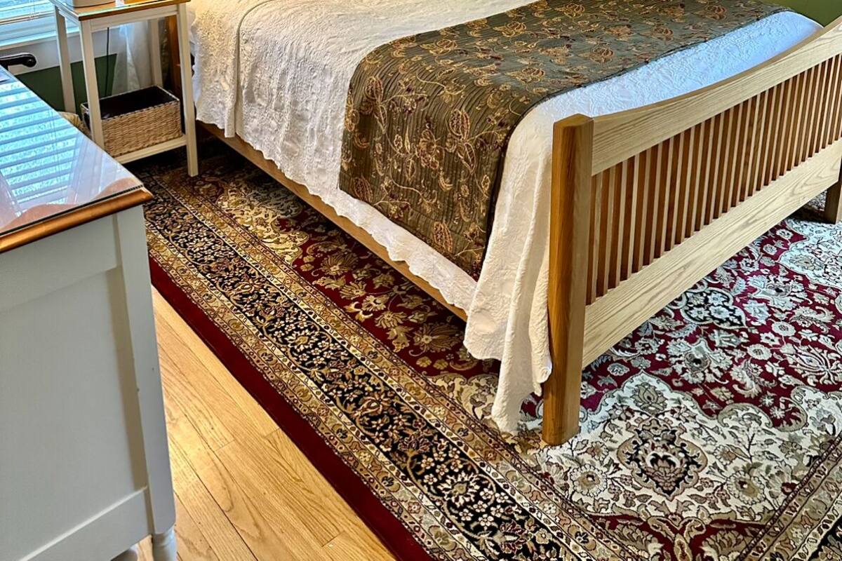 A bedroom with a wooden bed, two bedside tables, a nightstand, a patterned rug, and a stained glass window.