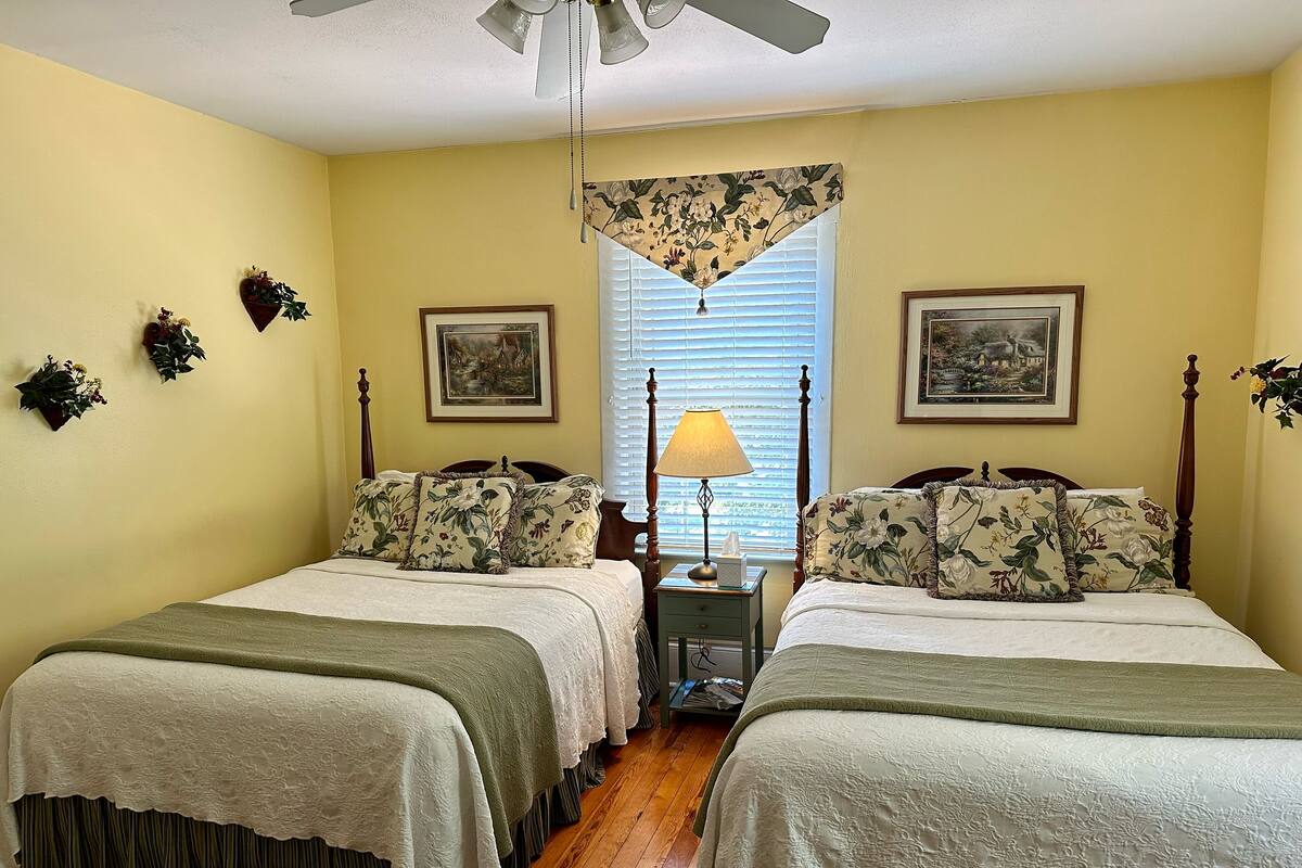 A bedroom with two beds, a nightstand with a lamp, and floral wall decorations.