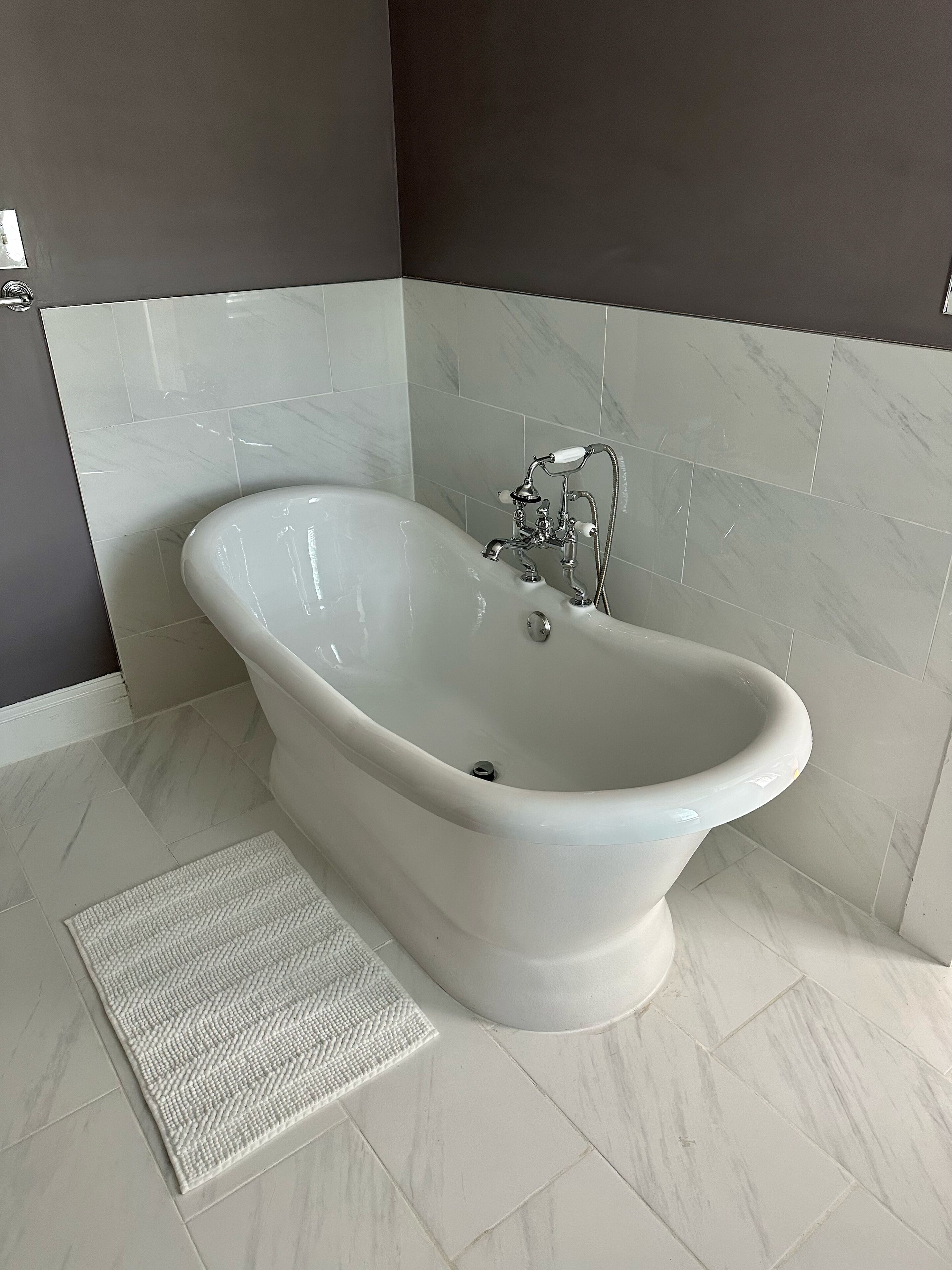 A modern bathroom with a freestanding bathtub, a showerhead, and a textured bath mat.