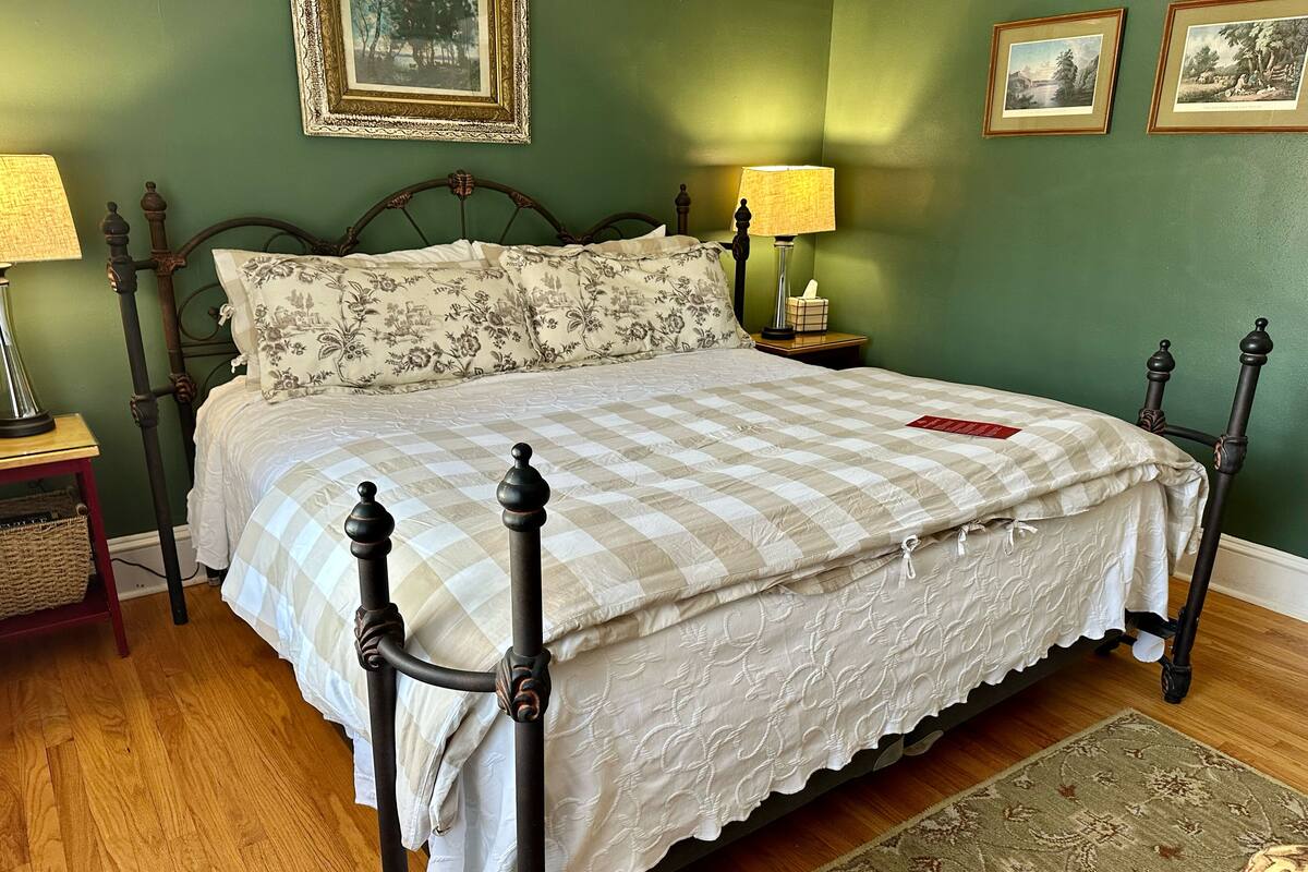 A neatly made bed with a checkered bedspread and a floral pillow, a bedside table with a lamp, and a framed picture on the wall.