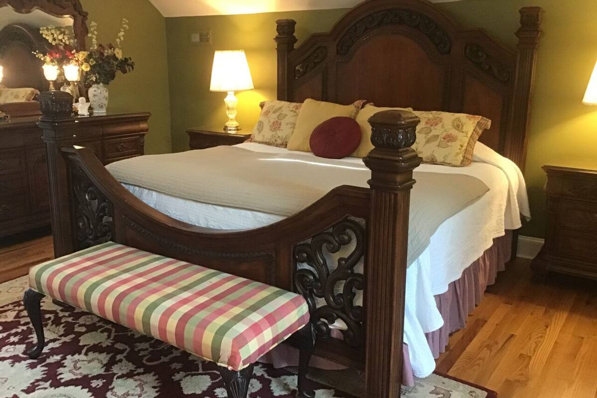 A bedroom with a four-poster bed, a bench, two bedside tables, and a mirror.