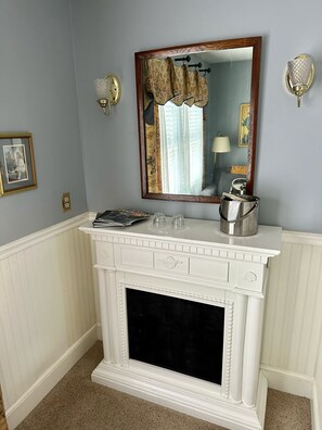 A room with a white fireplace, a mirror with a floral frame, and a wall-mounted lamp.