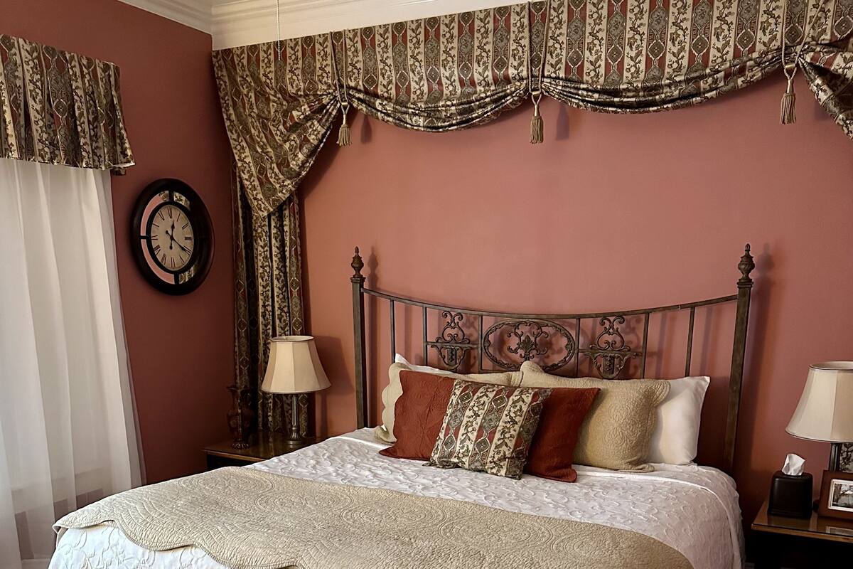 A bedroom with a large bed, a clock, and a nightstand with a lamp.
