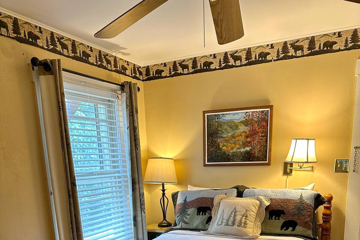 A four-poster bed with a quilt, a painting above it, and a lamp on the nightstand.