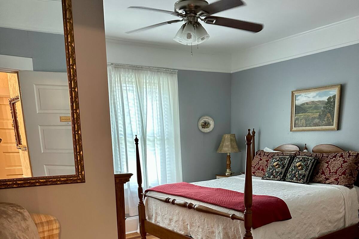 A bedroom with a four-poster bed, a wooden chair, a ceiling fan, and a rug.