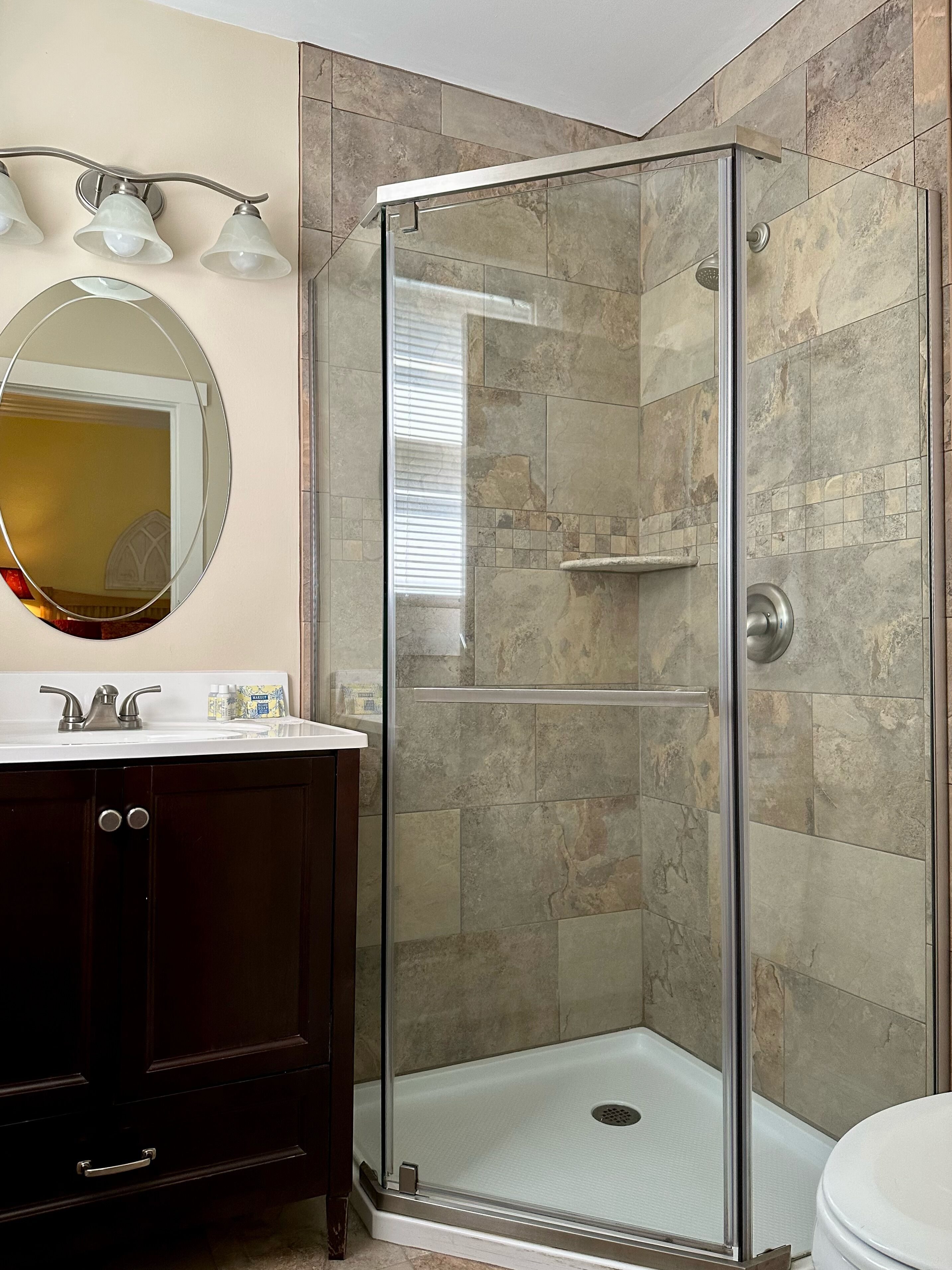 Une salle de bain avec une douche à parois de verre, un meuble-lavabo avec un miroir et des toilettes.