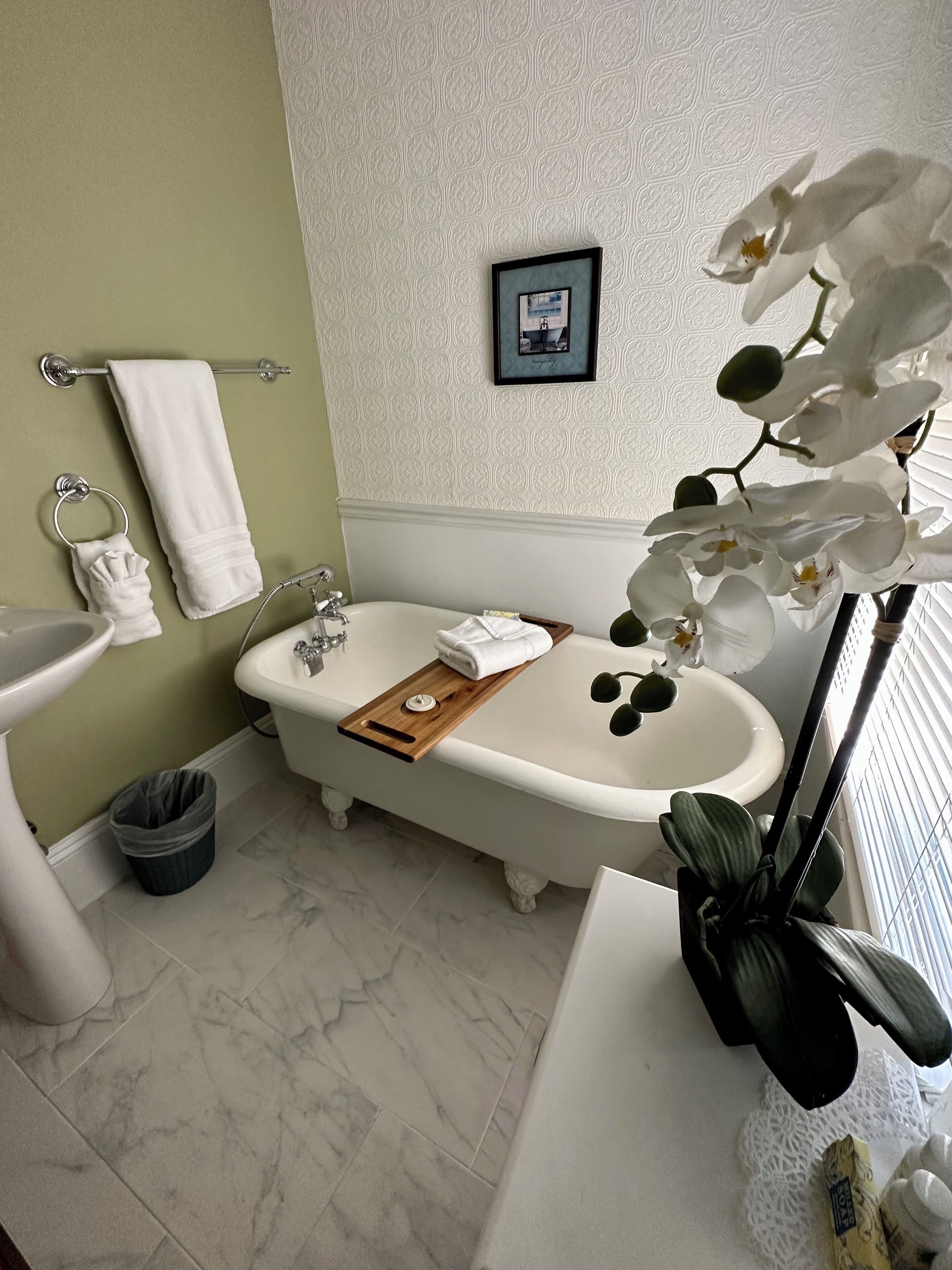 A bathroom with a freestanding bathtub, a sink, a towel rack, and a trash bin.