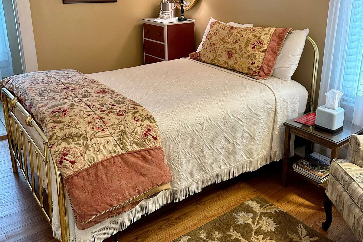 A bedroom with a bed, bedside table, lamp, and a mirror.