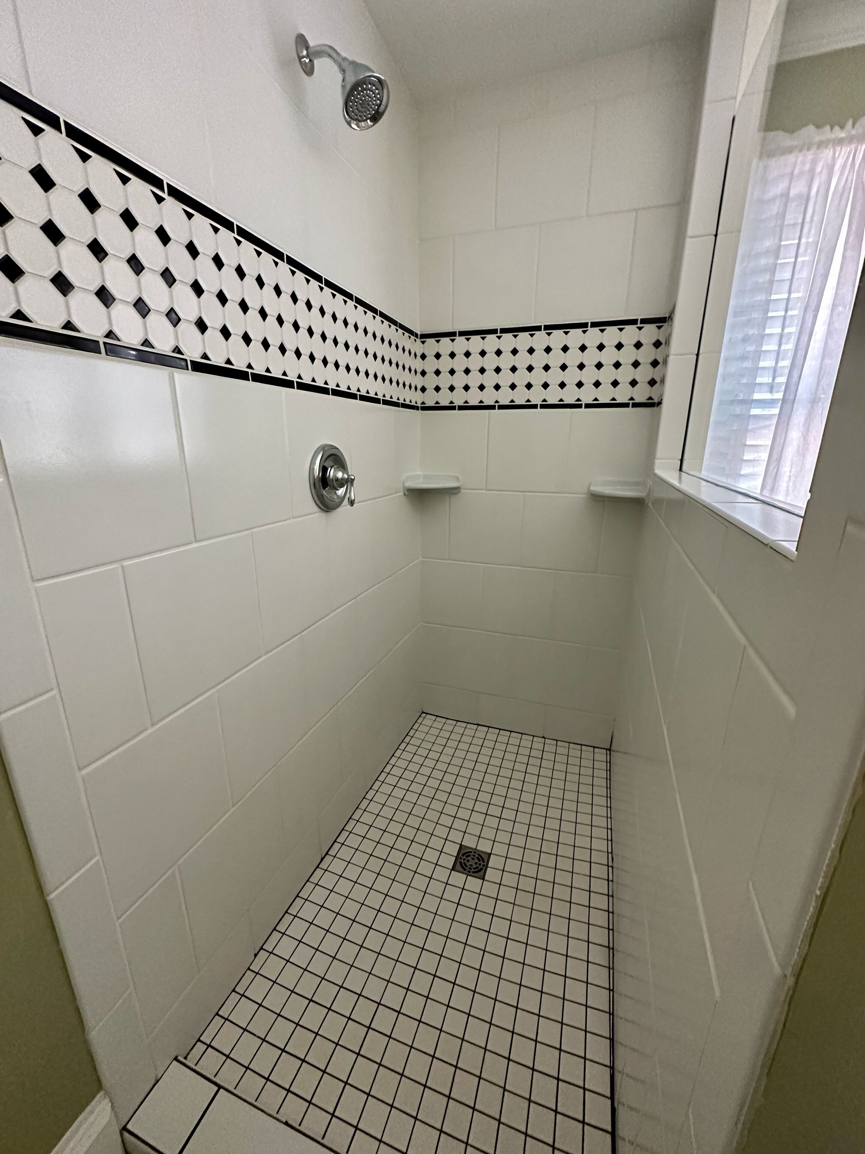 Une petite douche carrelée, avec un sol à carreaux et un motif losange noir et blanc sur les murs.