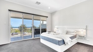 A modern bedroom with a large bed, a sliding glass door leading to a balcony, and a view of the sea.