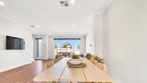 A modern dining area with a wooden table and chairs, a large bowl centerpiece, and a view of a balcony with palm trees.