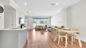 A modern kitchen with a built-in island, a dining area with wooden chairs and a table, and a living room with a sofa and a coffee table.