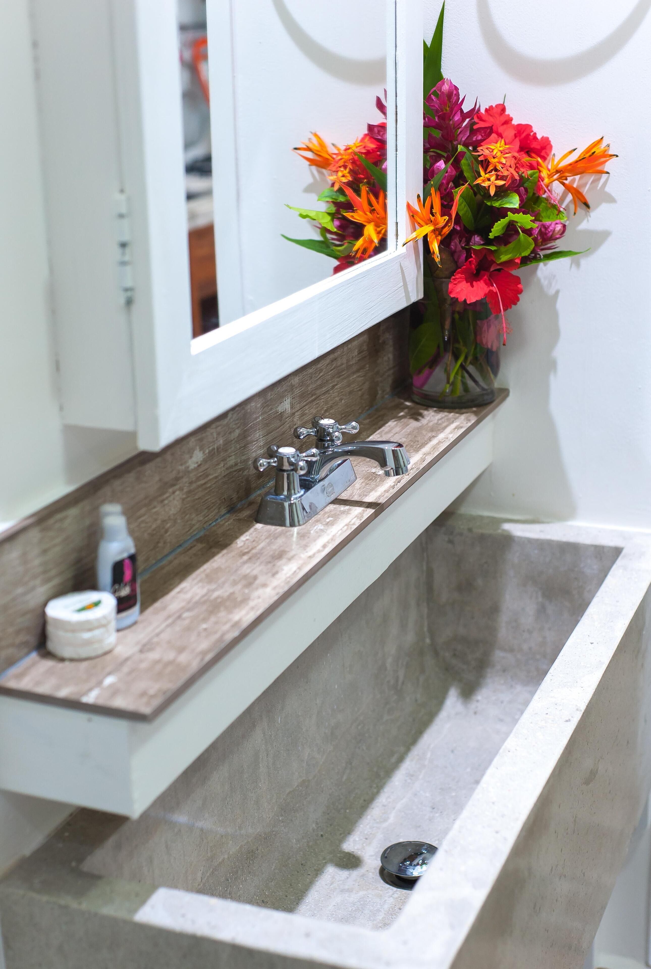 Un baño con un lavamanos moderno, un espejo y un florero con flores.