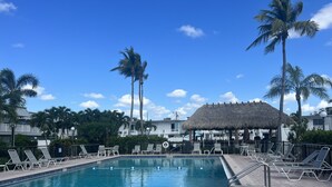 A swimming pool with lounge chairs and a thatched-roof structure. - Cozy and sweet condo . (Fort Myers)