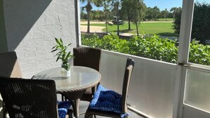 A covered patio with a round table and wicker chairs, overlooking a golf course. - Cozy and sweet condo . (Fort Myers)