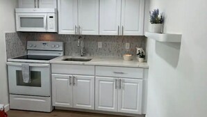 A modern kitchen with white cabinets, a microwave, an oven, and a sink. - Cozy and sweet condo . (Fort Myers)