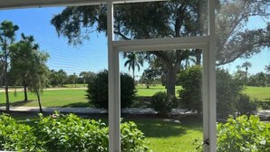 Vista desde una ventana que da a un campo de golf y árboles.