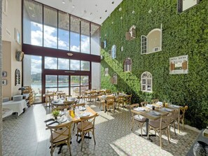 A restaurant with outdoor seating, large windows, and a green wall with window designs.