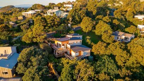 A large, multi-story house surrounded by dense trees, with a visible deck and a satellite dish. - The Kingfisher House - Oneroa (Waiheke Island)