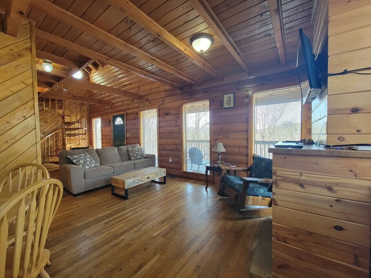 Interior acogedor de una cabaña con piso de madera, un sofá, una mesita de centro y un televisor fijado a la pared.