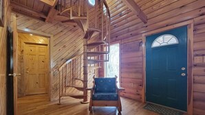 A wooden interior with a spiral staircase, a blue cushioned chair, and a green door. - Mountain Rose- Hot Tub, Pool Table, Firepit, Fireplace (Stanton)