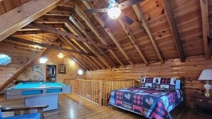 A cozy attic bedroom with a pool table, a bed with a quilt, and a ceiling fan. - Mountain Rose- Hot Tub, Pool Table, Firepit, Fireplace (Stanton)