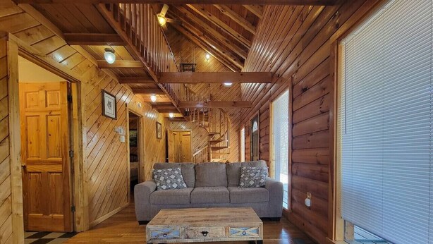 A wooden interior with a sofa and a coffee table, wooden floors, and a staircase. - Mountain Rose- Hot Tub, Pool Table, Firepit, Fireplace (Stanton)